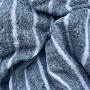 May include: Close-up of a blue and white striped fabric with a textured weave. The fabric is folded and wrinkled, creating a dynamic pattern.
