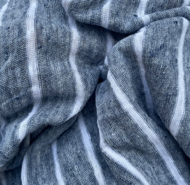 May include: Close-up of a blue and white striped fabric with a textured weave. The fabric is folded and wrinkled, creating a dynamic pattern.