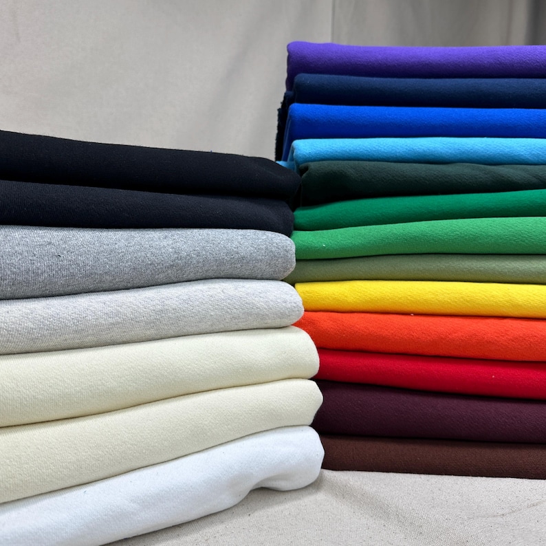 May include: Stacks of colorful fabric in various shades, including black, gray, cream, and a rainbow of hues. The fabric appears to be a soft, possibly knit material, neatly folded and stacked. The image showcases a variety of colors.