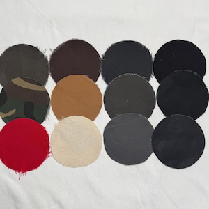 Puede incluir: Una colecci&oacute;n de doce parches de tela circulares dispuestos en una cuadr&iacute;cula. Los parches presentan varios colores s&oacute;lidos, incluyendo negro, gris oscuro, marr&oacute;n, beige, rojo y crema, junto con un parche con un patr&oacute;n de camuflaje verde, marr&oacute;n y negro.