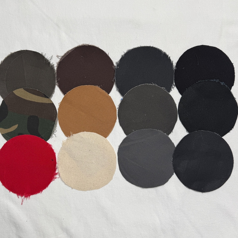Puede incluir: Una colecci&oacute;n de doce parches de tela circulares dispuestos en una cuadr&iacute;cula. Los parches presentan varios colores s&oacute;lidos, incluyendo negro, gris oscuro, marr&oacute;n, beige, rojo y crema, junto con un parche con un patr&oacute;n de camuflaje verde, marr&oacute;n y negro.
