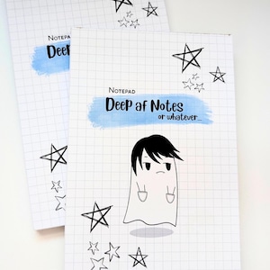 May include: Two rectangular notepads with a white grid pattern background. Each features a blue watercolor-style brushstroke with the text "Notepad Deep af Notes or whatever..." and a cartoon ghost illustration surrounded by hand-drawn black stars.