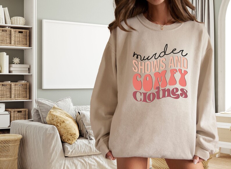 May include: A beige sweatshirt with the text "murder shows and comfy clothes" printed in black and pink.