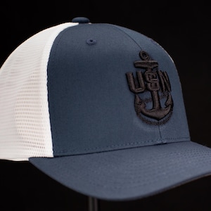 May include: A navy blue and white mesh baseball cap with a black embroidered US Navy anchor logo.