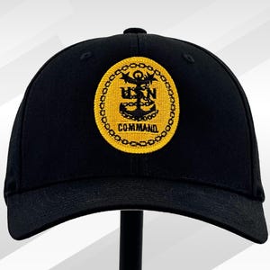 May include: Black baseball cap with a yellow embroidered patch featuring a US Navy anchor and the text "COMMAND".