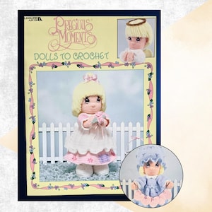 May include: A Leisure Arts Precious Moments Dolls to Crochet pattern book featuring a blonde doll in a pink and white dress, an angel doll with a halo, and a doll in a blue bonnet. The cover includes floral borders and white picket fence imagery.