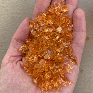 May include: A handful of small, translucent orange glass pieces. The pieces are irregular in shape and have a slightly iridescent sheen.