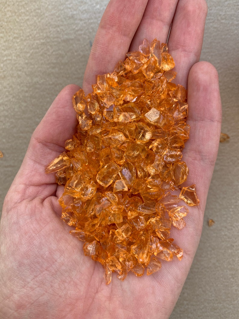 May include: A handful of small, translucent orange glass pieces. The pieces are irregular in shape and have a slightly iridescent sheen.
