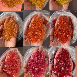 May include: Four bags of crushed glass, each containing a different colour: amber, orange, red, and green. The glass is in small, irregular pieces.
