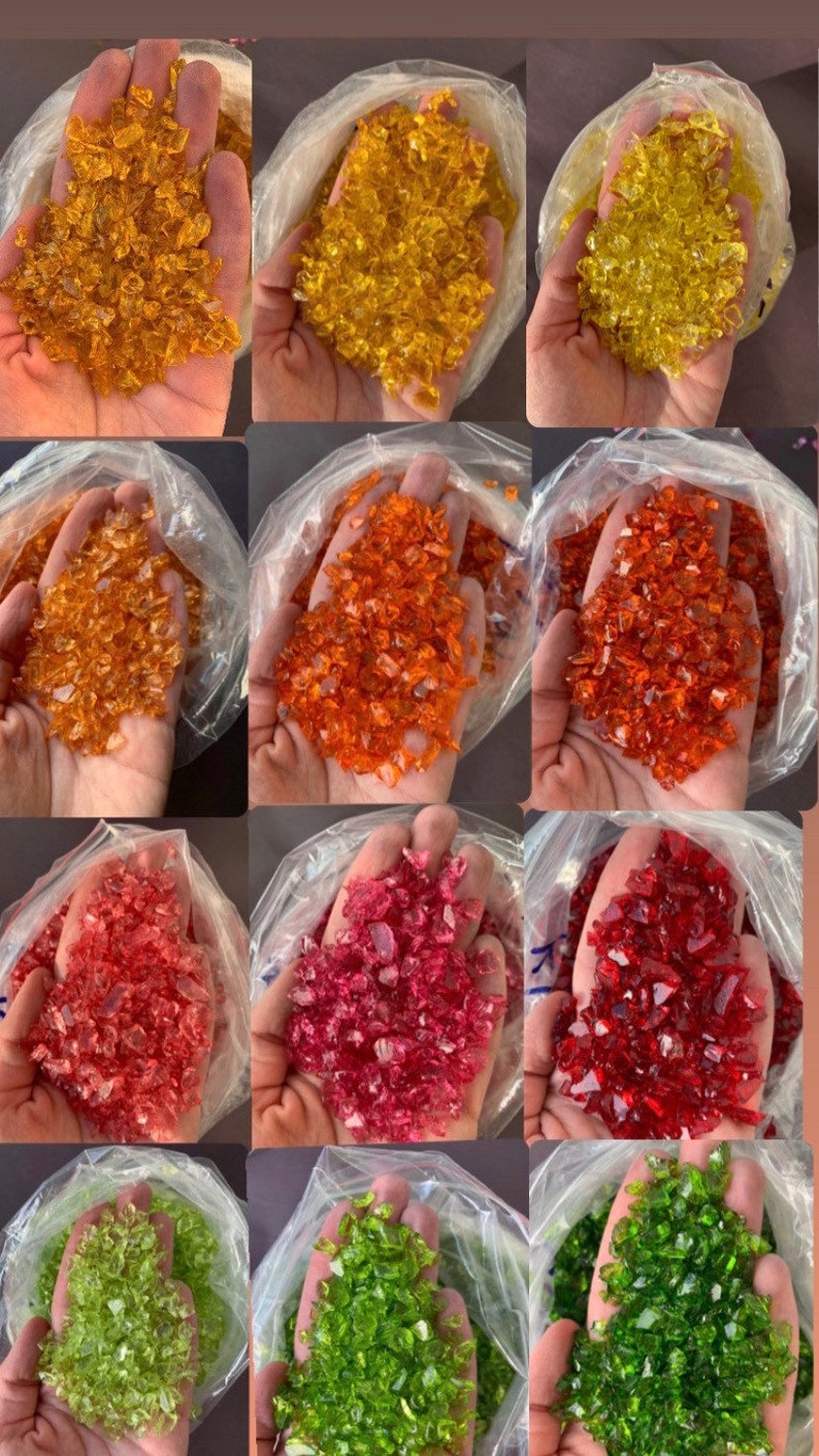 May include: Four bags of crushed glass, each containing a different colour: amber, orange, red, and green. The glass is in small, irregular pieces.