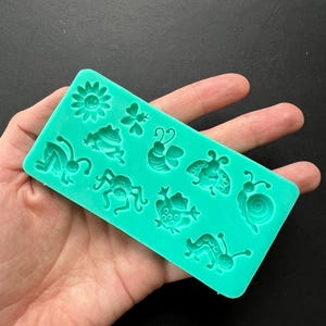 May include: Green silicone mold with various animal and flower shapes. The mold includes a frog, a bee, a ladybug, a snail, a spider, a caterpillar, a flower, and a butterfly.