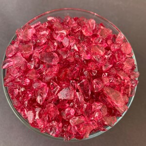 May include: A glass bowl filled with small, pink, iridescent glass pieces. The glass pieces are irregular in shape and size.