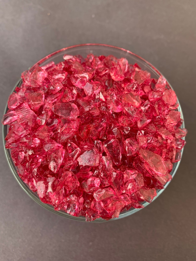 May include: A glass bowl filled with small, pink, iridescent glass pieces. The glass pieces are irregular in shape and size.