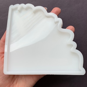 May include: White silicone mold for resin casting, shaped like a corner with a wavy edge.