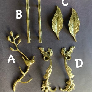 May include: Assortment of six gold-toned cabinet hardware pulls. Two are simple bamboo-style pulls, two are ornate leaf-shaped pulls, and two are ornate scroll-shaped pulls.