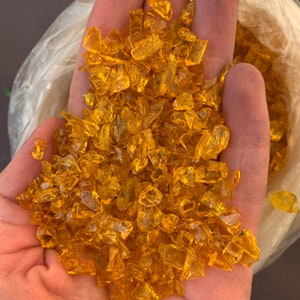 May include: A handful of small, clear, amber-coloured glass pieces. The glass pieces are irregular in shape and have a slightly iridescent sheen.