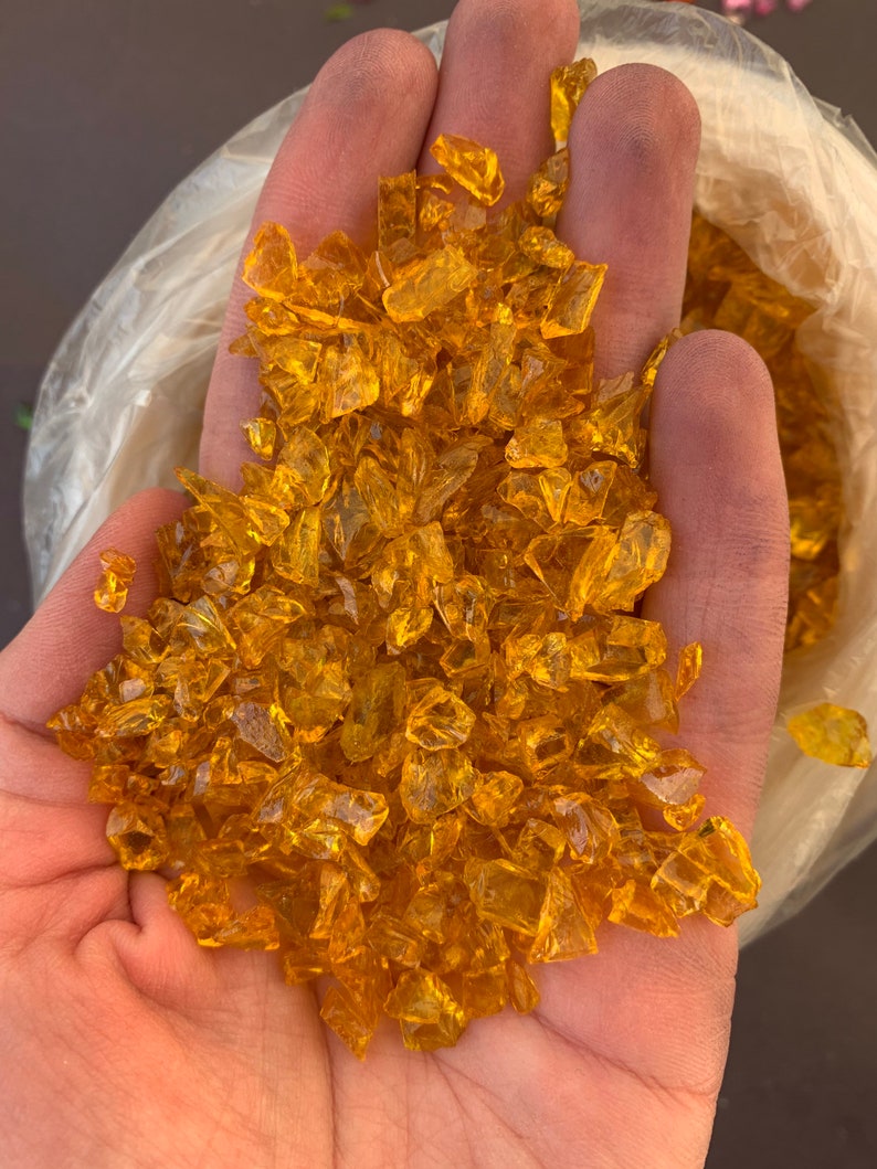 May include: A handful of small, clear, amber-coloured glass pieces. The glass pieces are irregular in shape and have a slightly iridescent sheen.