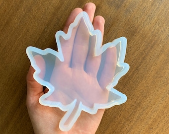 Puede incluir: Un molde de silicona transparente con forma de hoja de arce. El molde es flexible y tiene una superficie lisa.