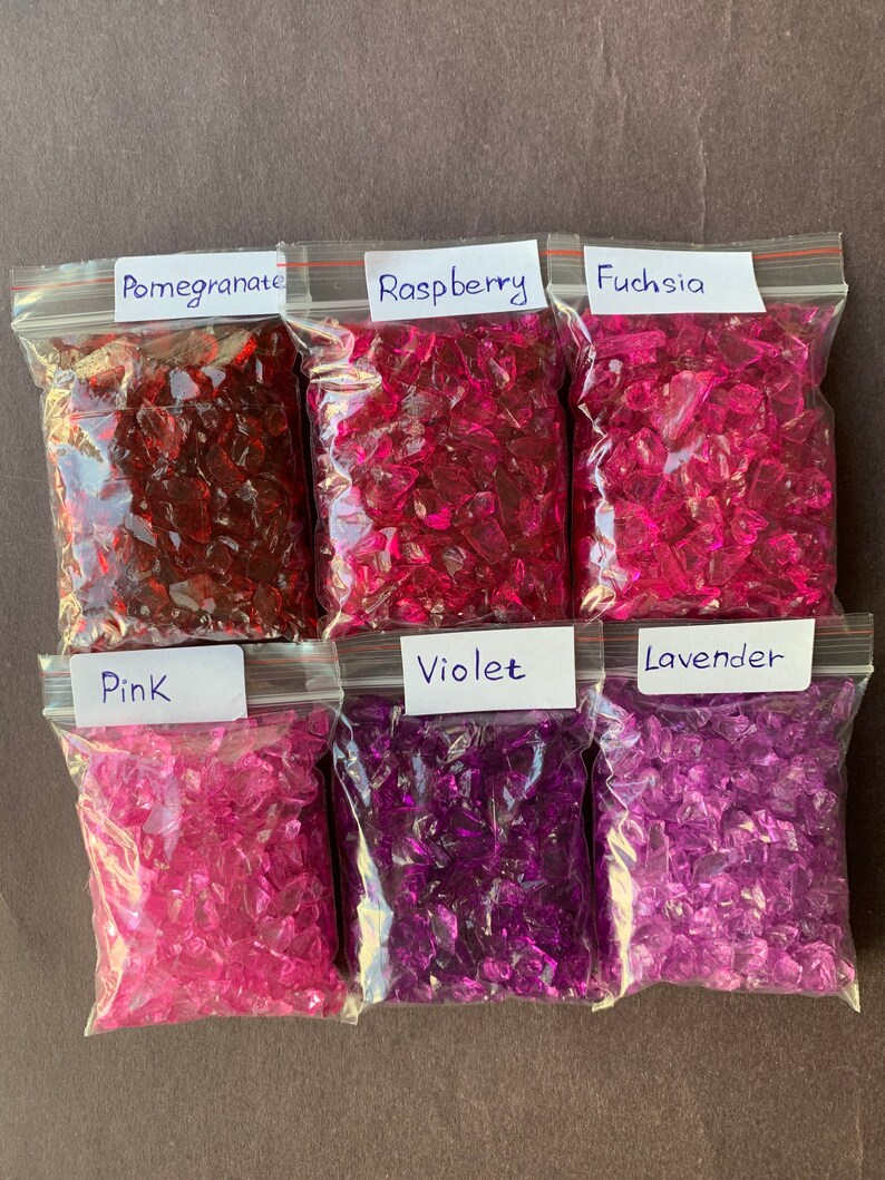 May include: Six clear plastic bags filled with crushed glass, each bag labeled with a color name: Pomegranate, Raspberry, Fuchsia, Pink, Violet, and Lavender.