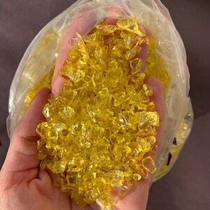 May include: A bag of yellow glass chips. The chips are small and irregular in shape. They are ideal for crafts or home decor.
