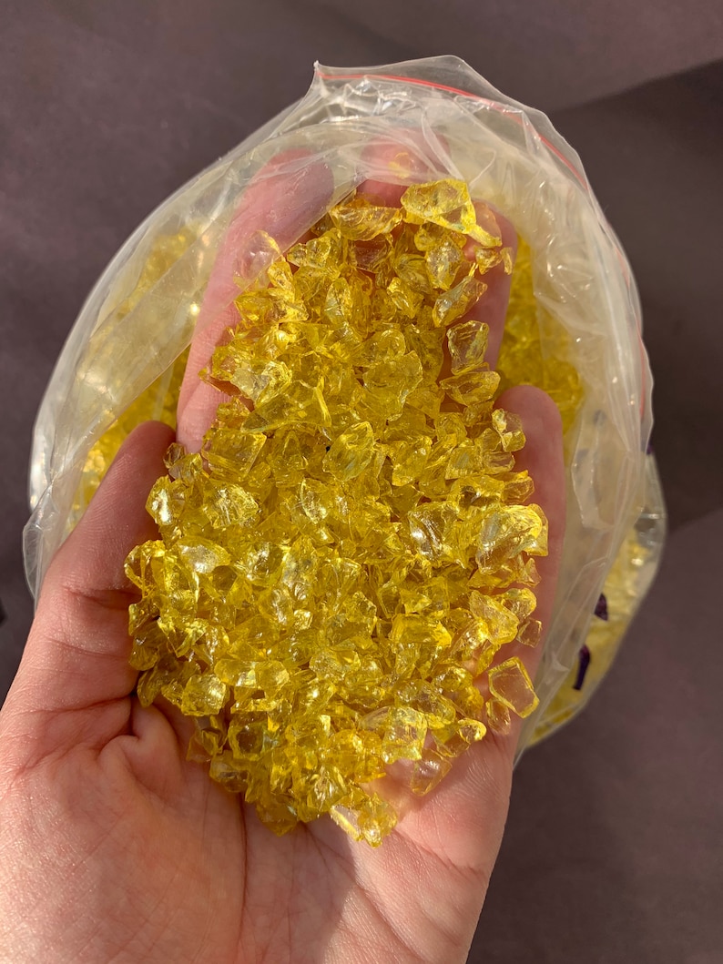 May include: A bag of yellow glass chips. The chips are small and irregular in shape. They are ideal for crafts or home decor.