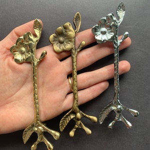 May include: Three decorative metal flower-shaped handles in gold and silver. The handles have a stylized floral design with a flower at the top and a three-pronged base.