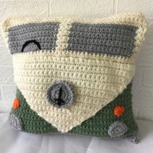May include: A crocheted pillow in the shape of a vintage camper van. The camper is green with white details and orange accents.