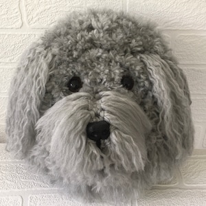 May include: A grey fluffy dog head wall decoration. The dog has black eyes and a black nose.