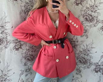 May include: A coral pink blazer with a double breasted closure, white buttons, and a black belt. The blazer has a relaxed fit and is made of a lightweight fabric.
