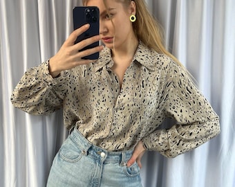 May include: A woman wearing a beige and black animal print button-down shirt with long sleeves and light blue jeans.