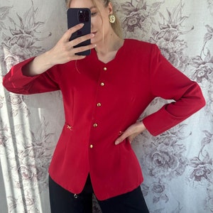 Puede incluir: Una chaqueta roja con botones dorados y un detalle de cadena dorada en la cintura.