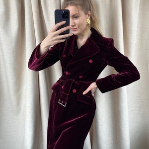 May include: A long, burgundy velvet coat with a double-breasted closure, a belt, and two front pockets.