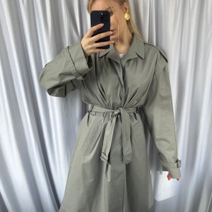 May include: A gray trench coat with a belt and long sleeves. The coat has a button closure and a collar.