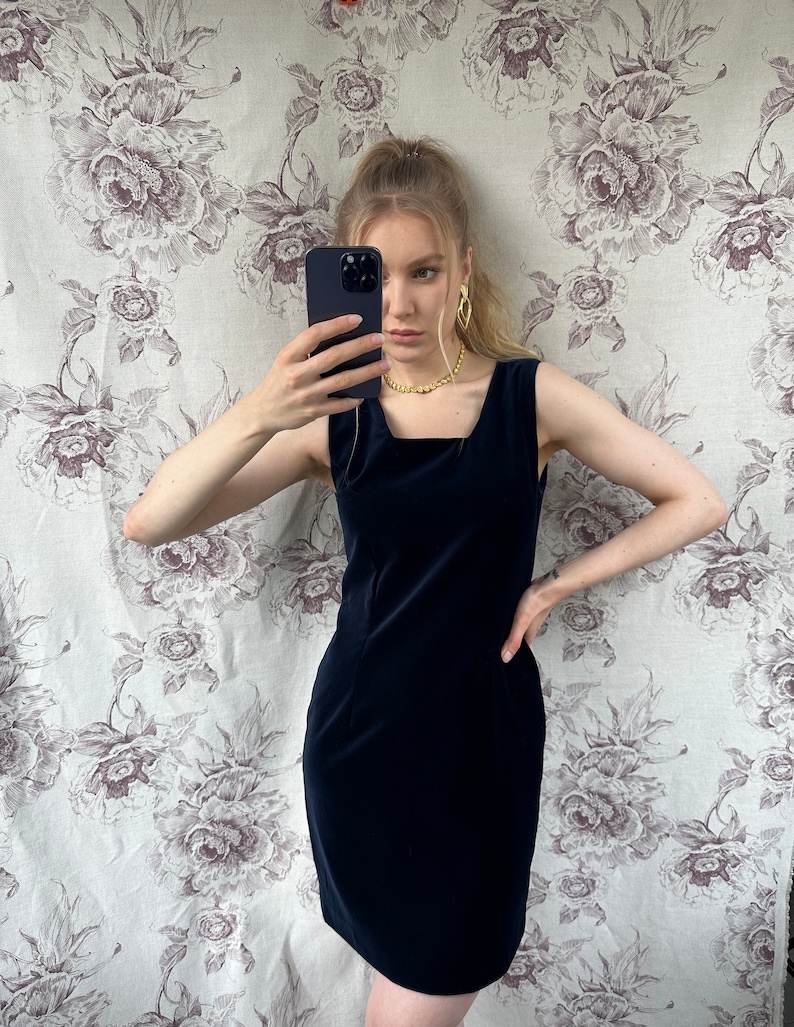 Pu&ograve; includere: Un abito in velluto blu navy senza maniche con scollo quadrato. L'abito &egrave; aderente e ha una lunghezza corta.