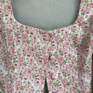 May include: Close-up of the front of a pink and green floral print top with a button closure. The top has a square neckline and a fitted bodice.