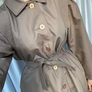 May include: A brown trench coat with a belt and buttons. The coat has a classic design and is made of a durable fabric.