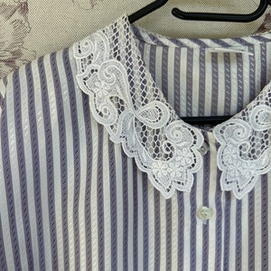 Pode incluir: Uma blusa listrada branca e roxa com uma gola de renda branca. A gola tem uma borda festonada e um design floral.