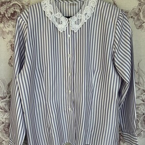 Pode incluir: Uma camisa de manga comprida listrada em branco e roxo com uma gola de renda branca.