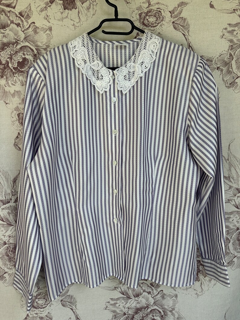 Pode incluir: Uma camisa de manga comprida listrada em branco e roxo com uma gola de renda branca.