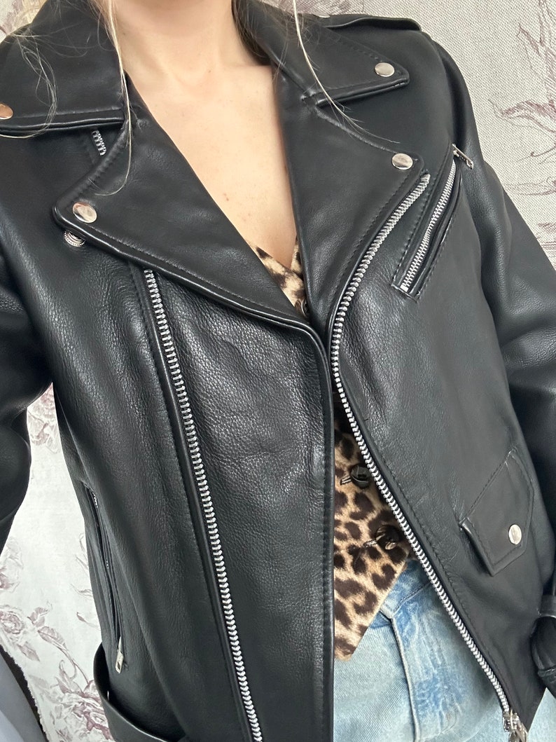 May include: A black leather motorcycle jacket with a zipper closure and silver hardware. The jacket has a classic biker style with a pointed collar and a zippered pocket on the left sleeve.