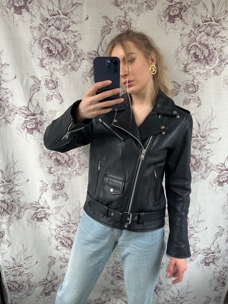 May include: A black leather motorcycle jacket with a zipper closure and a belt at the waist. The jacket has a  stand-up collar and long sleeves.