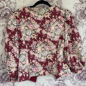 May include: A maroon floral print jacket with a slightly puffed sleeve. The jacket has a V-neck and a fitted silhouette.