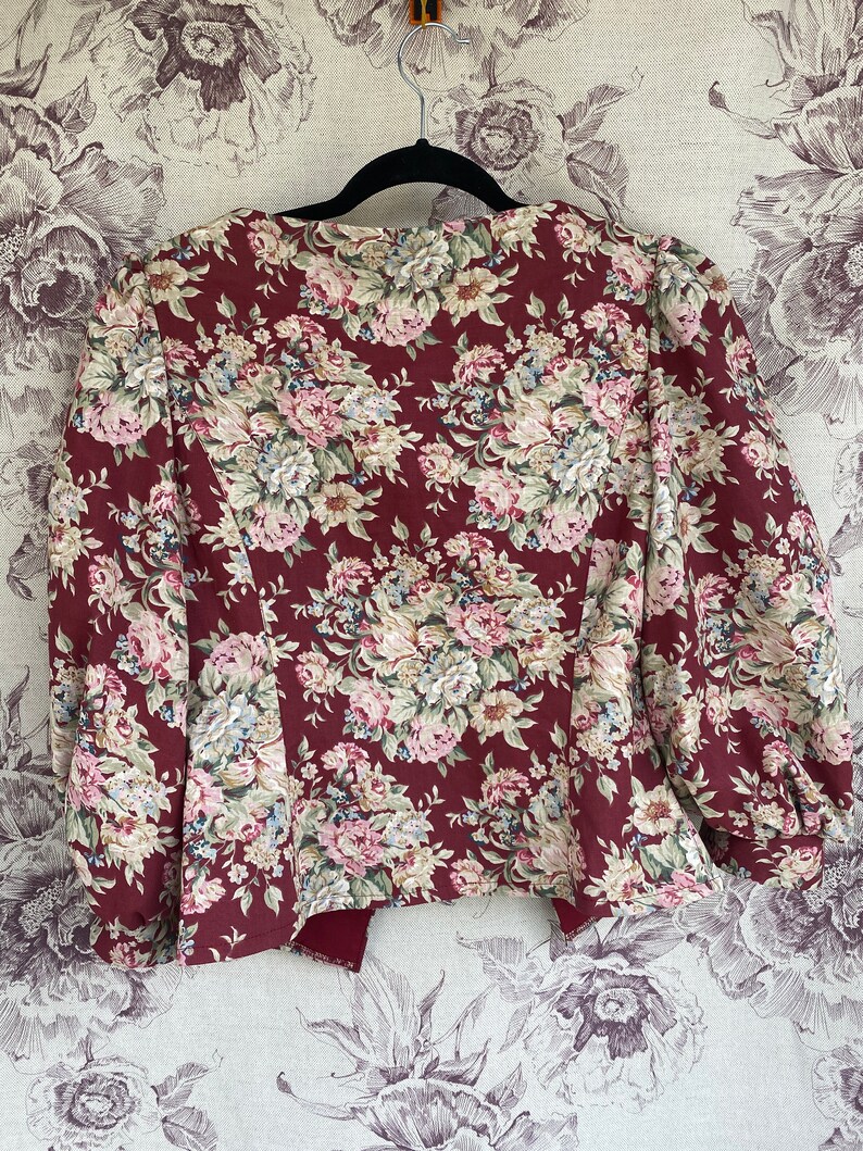 May include: A maroon floral print jacket with a slightly puffed sleeve. The jacket has a V-neck and a fitted silhouette.