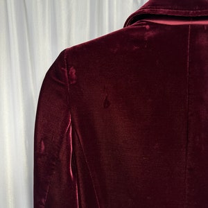 May include: A deep burgundy velvet blazer with a classic collar and long sleeves. The blazer is made of a soft, luxurious fabric and has a smooth, polished finish.