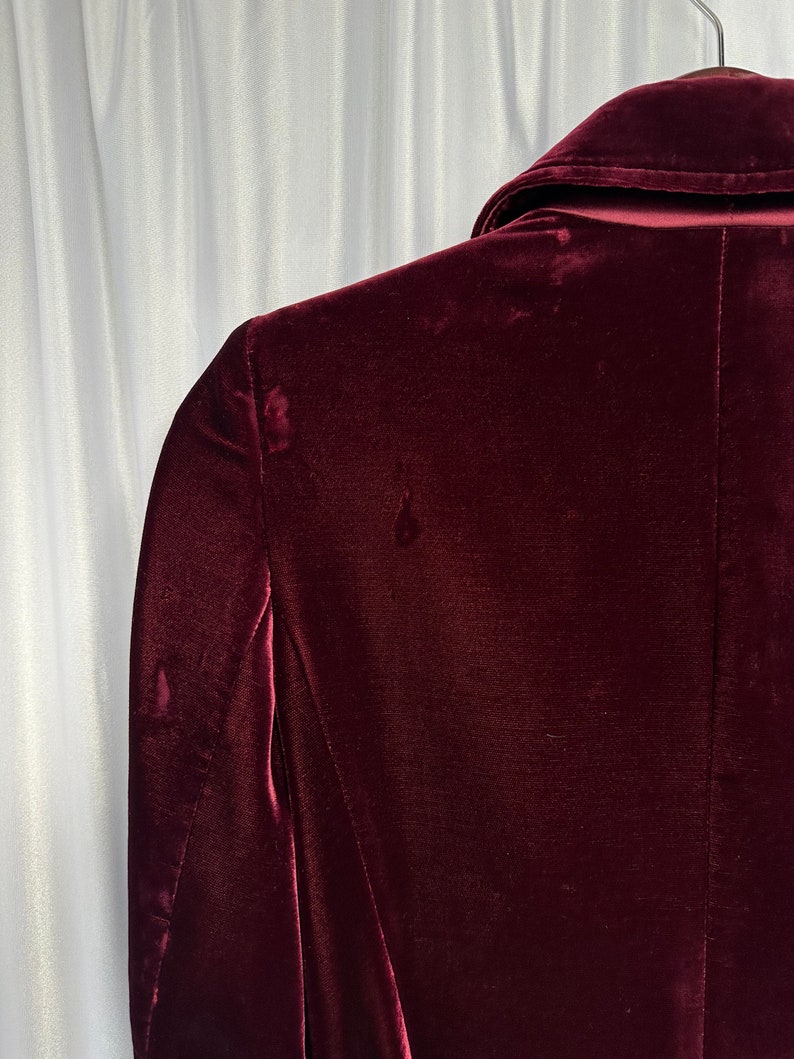 May include: A deep burgundy velvet blazer with a classic collar and long sleeves. The blazer is made of a soft, luxurious fabric and has a smooth, polished finish.