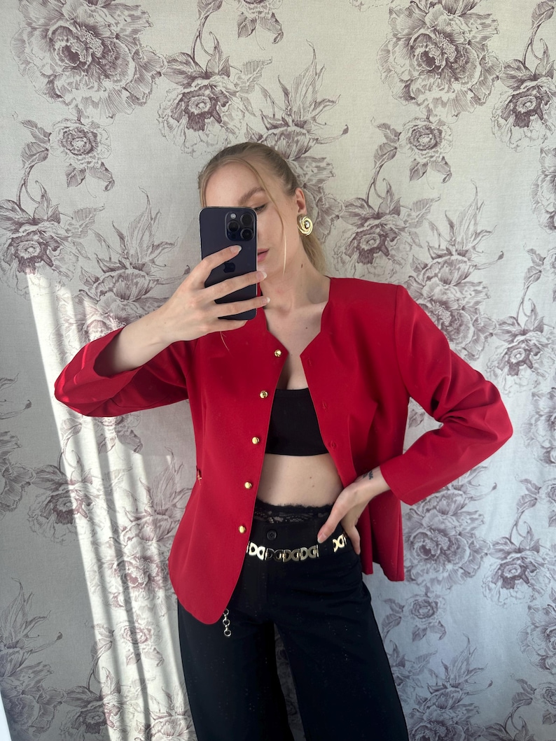 Puede incluir: Una chaqueta roja con botones dorados y un cintur&oacute;n de cadena dorada. La chaqueta tiene mangas largas y cuello en V.