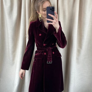 May include: A long, burgundy velvet coat with a double-breasted closure, a belt, and two front pockets.