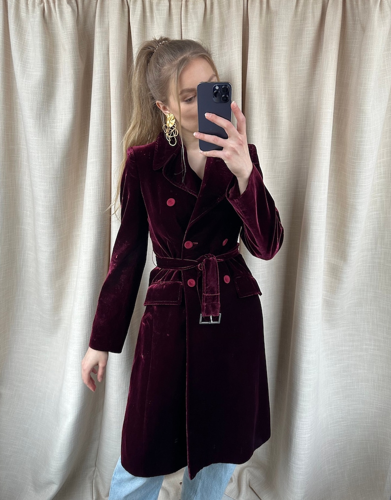 May include: A long, burgundy velvet coat with a double-breasted closure, a belt, and two front pockets.