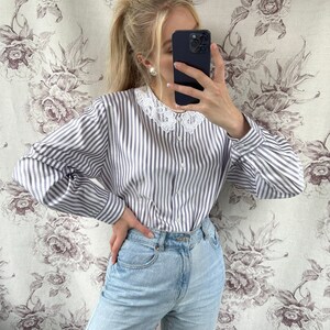 Pode incluir: Uma camisa de manga comprida listrada azul e branca com uma gola de renda branca. A camisa &eacute; usada com jeans azul claro.