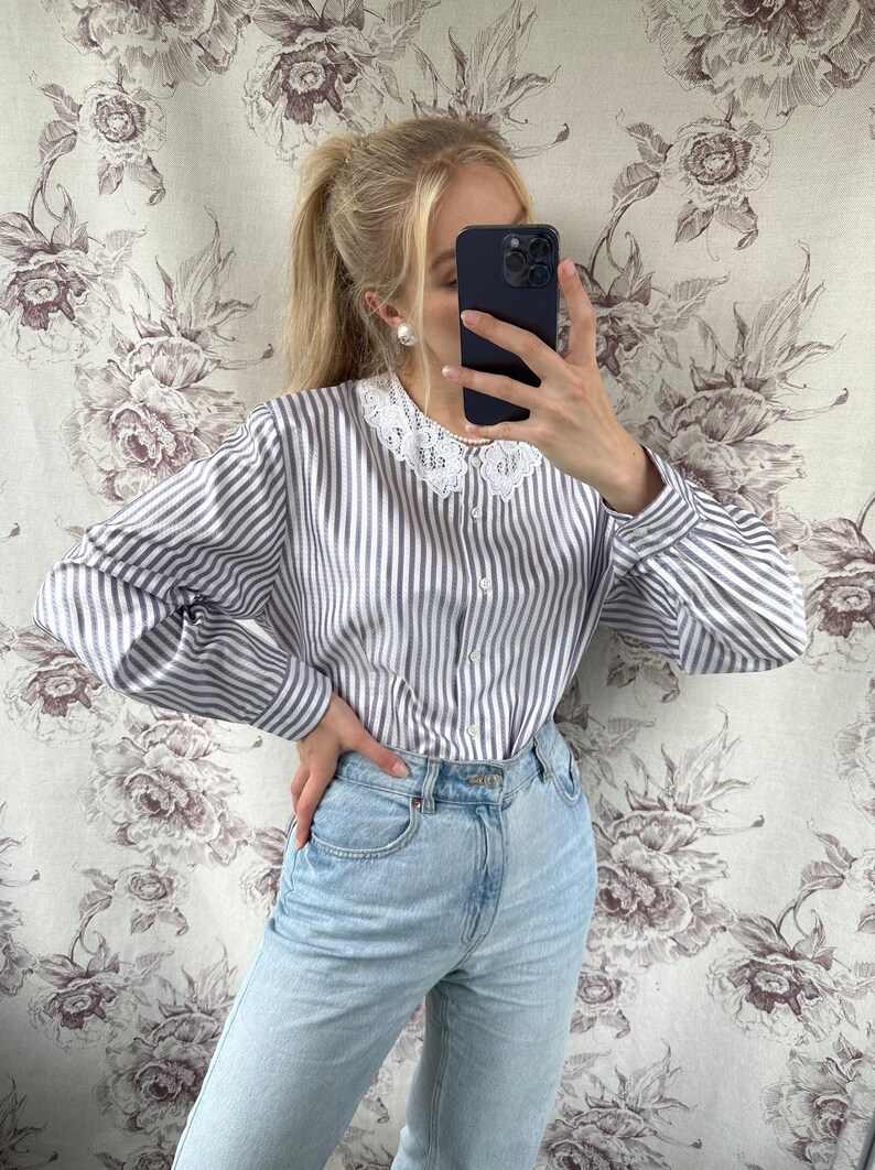 Pode incluir: Uma camisa de manga comprida listrada azul e branca com uma gola de renda branca. A camisa &eacute; usada com jeans azul claro.